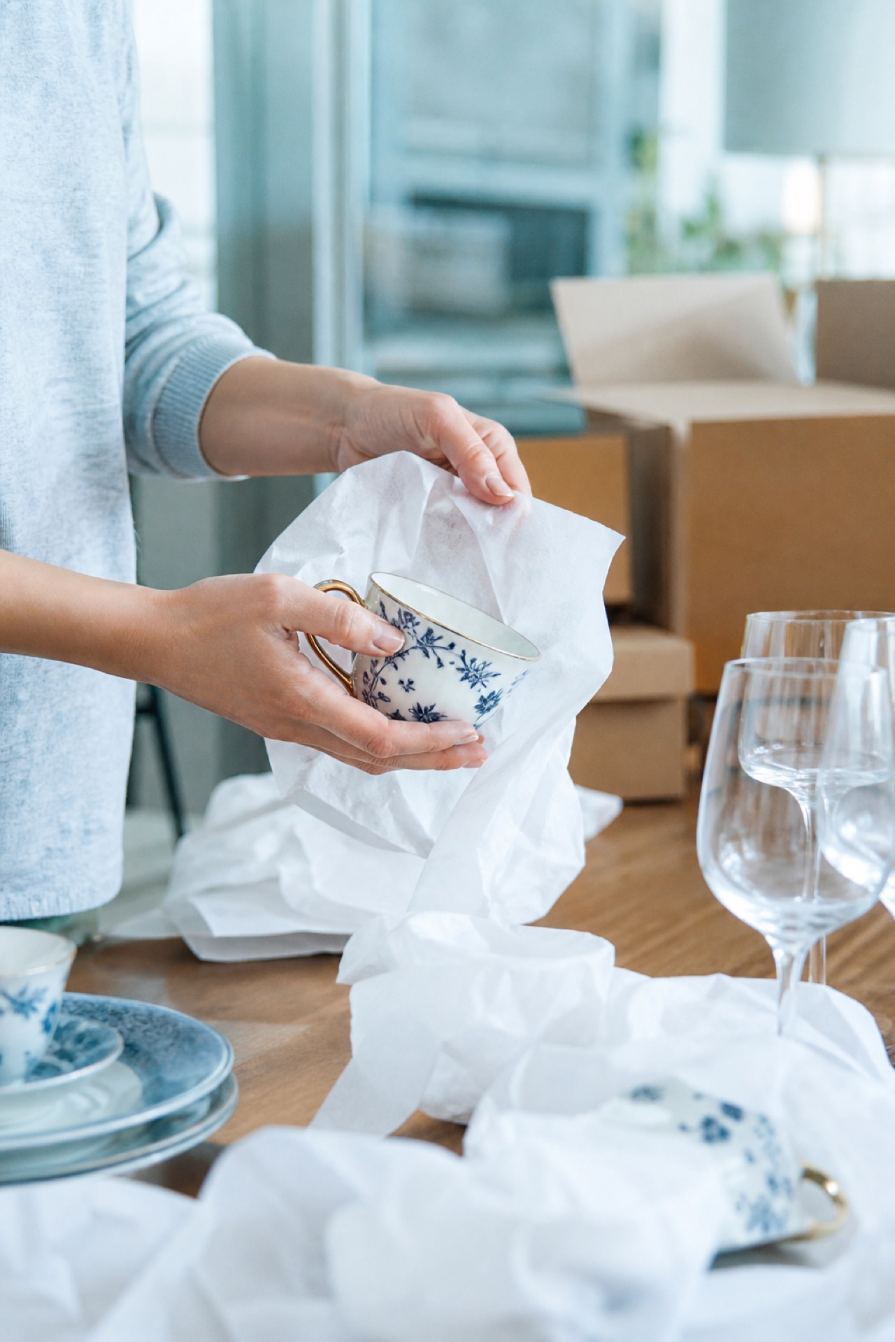 Hände wickeln empfindliches Porzellan sorgfältig in Seidenpapier